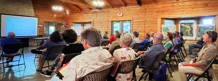 A person giving a presentation to a group of people at a public meeting at Davis Lodge.