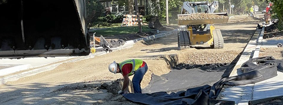 Person standing in large hole in a rock road base with a loader preparing to dump rock into it
